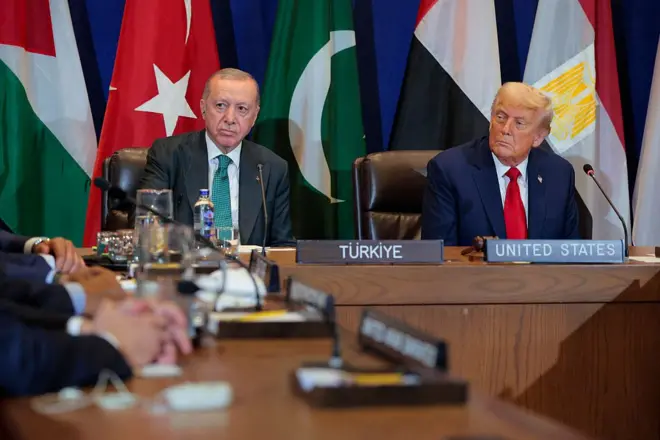 Erdoğan ve Trump kameralara bakıyor, arkada çeşitli ülke bayrakları var