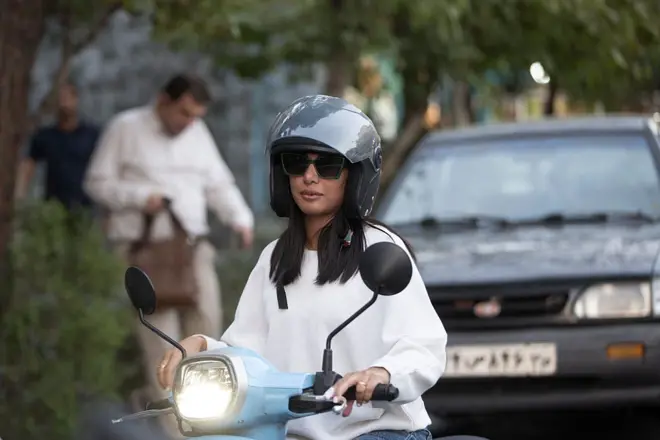 زن ایرانی با لباس سفید سوار بر موتور سیکلت آبی رنگ