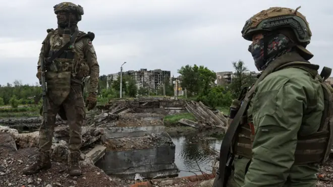 Двое российских военных в камуфляже на фоне разгромленного города