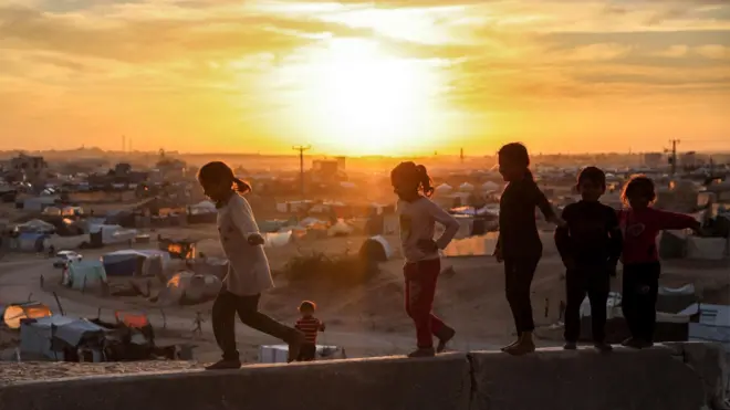 أطفال يمشون على حافة بالقرب من خيام تؤوي فلسطينيين نزحوا بسبب الصراع في مجمع مدينة حمد السكنية في شمال خان يونس في جنوب قطاع غزة في 22 ديسمبر/ كانون الأول 2024.