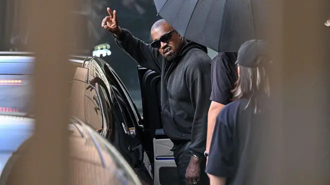 Kanye West for front of car wit Umbrella wey block half im face as e dey wave for China