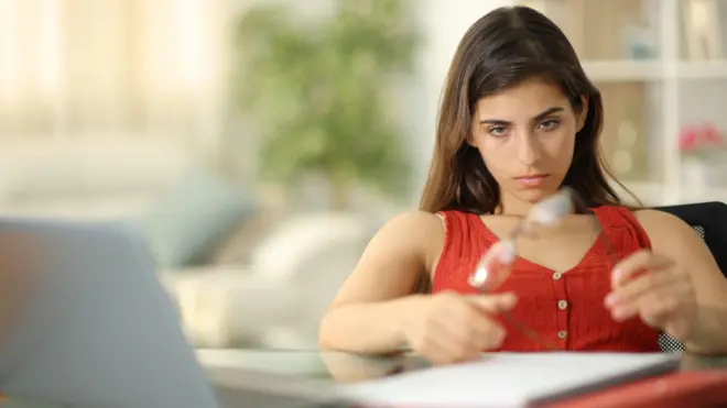 فتاة تجلس على كرسي وتنظر إلى نظارة بين يديها