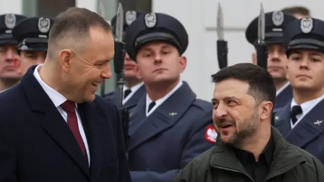 Dwóch mężczyzn śmieje się do siebie, podczas gdy żołnierze stoją na baczność za nimi