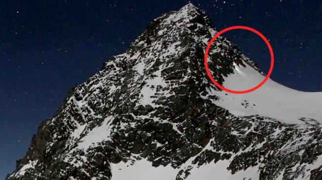 Mountain against a night sky with a red circle highlighting torchlight on the side of the mountain.