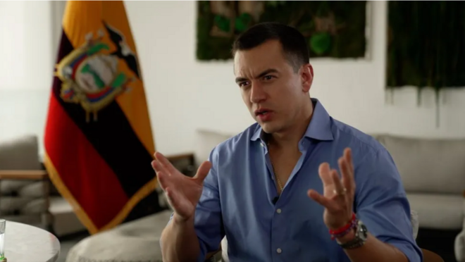 Noboa gesticulando durante entrevista em sala, com bandeira do Equador atrás