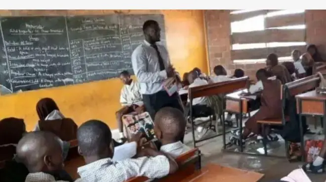 Olukọ kan duro, o n ba awọn akẹkọọ to jokoo sọrọ