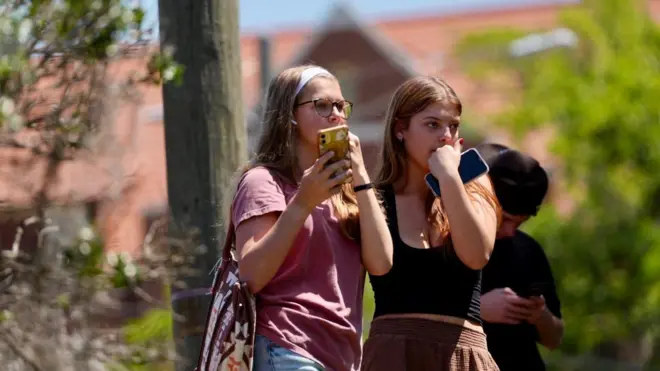 銃撃現場から避難した女子学生2人が、緊張した様子で警察の捜査を見守っている