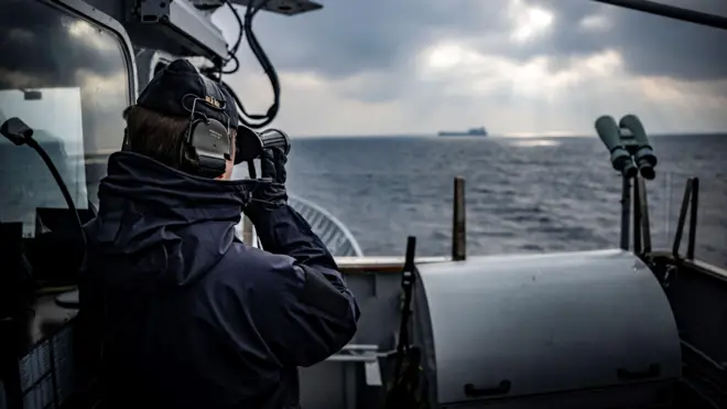 Un miembro de la tripulación del buque patrullero HSwMS Carlskrona observa un buque de carga en el horizonte a través de binoculares. 