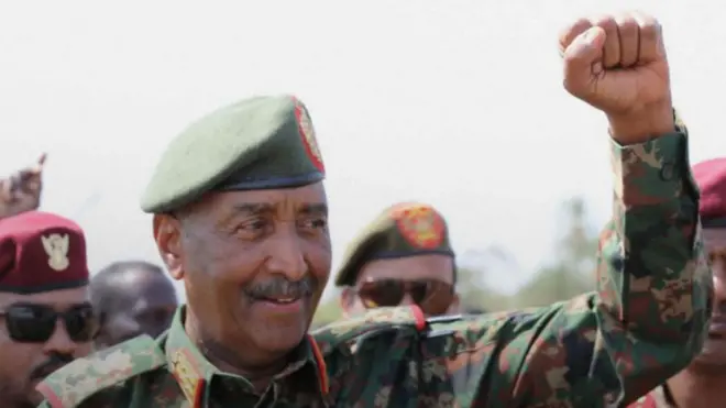 عبدالفتاح البرهان مرتدياً لباسه العسكري وملوحاً بيده وحوله عدد من الضباط