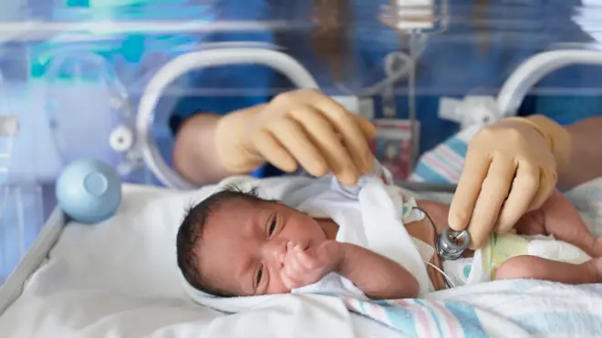 Female doctor examining newborn baby in incubator