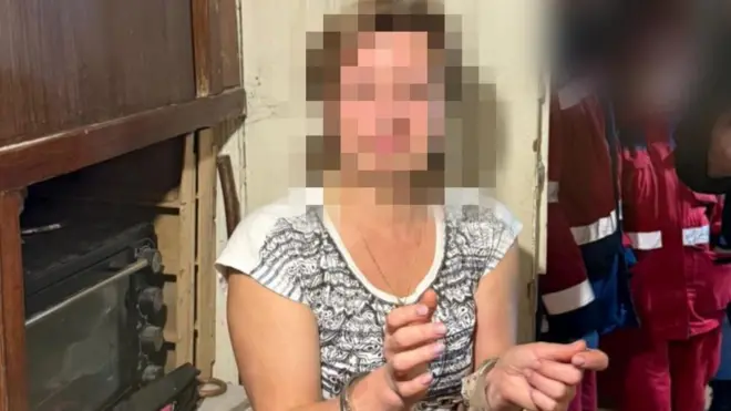 Жінка стоїть в кімнаті й жестикулює руками 