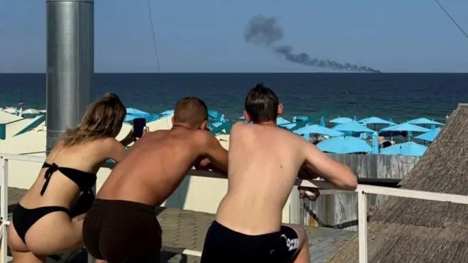 turistas observan un barco tanque envuelto en humo 