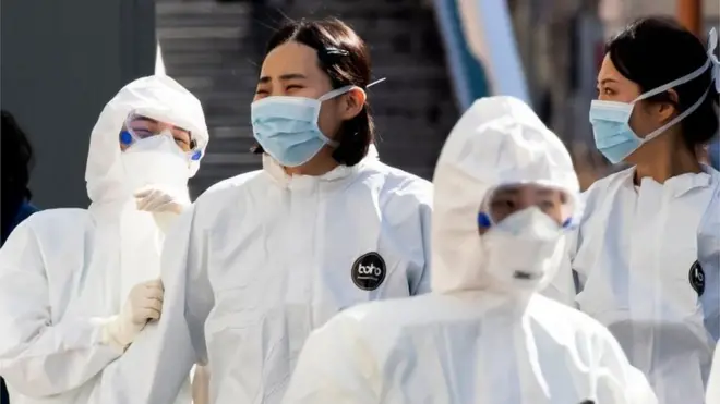 Dengan memakai baju pelindung, para staf medis tiba untuk merawat para pasoen Covid-19 di Daegu, kawasan terpapar virus corona paling parah di Korsel.