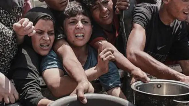 Palestinians hold out pots and bowls, jostling to reach the front of a line as they await meals distributed by aid groups in Gaza City