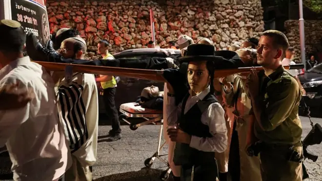 Jewish worshippers and rescue workers carry injured people outside a synagogue where a grandstand collapsed during a religious celebration in Givat Zeev, in the occupied West Bank, May 16, 2021