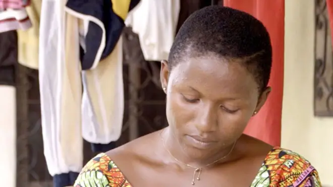 A woman with short hair and a patterned dress glances down.