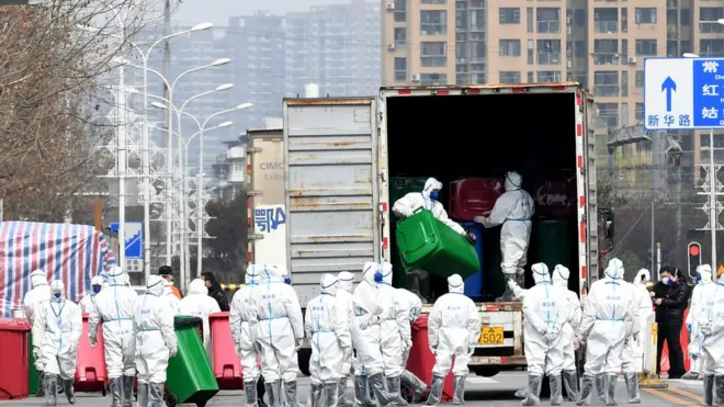 عمال يرتدون بذلات واقية يشاركون في تطهير سوق المأكولات البحرية في هوانان، حيث يُعتقد أن فيروس كورونا الجديد ظهر لأول مرة ، في ووهان بمقاطعة هوبي