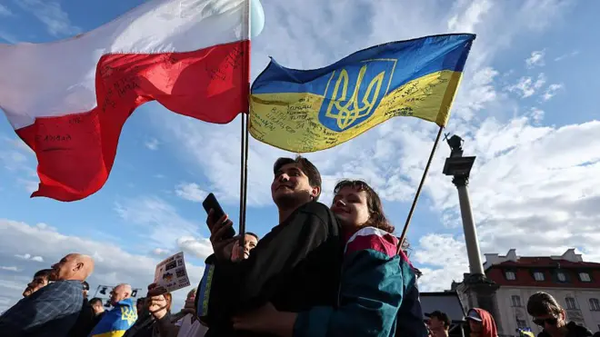 Mężczyzna i kobieta obejmują się podczas demonstracji na Placu Zygmunta w Warszawie. Nad ich głowami powiewa biało-czerwona flaga Polski i niebiesko-żółta flaga Ukrainy.