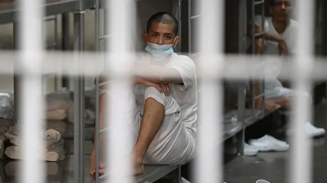 鉄格子越しに、ベッドに座っている収容者を写した写真