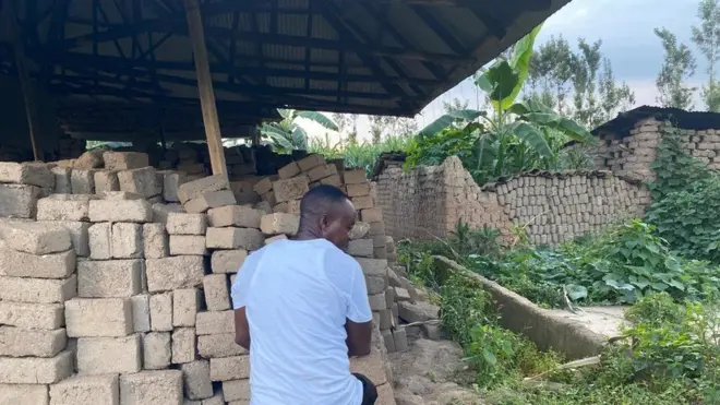 Charles Munyagisenyi ahagaze imbere y'ibyasigaye ku nzu ye yasenywe n'imyuzure mu mwaka ushize