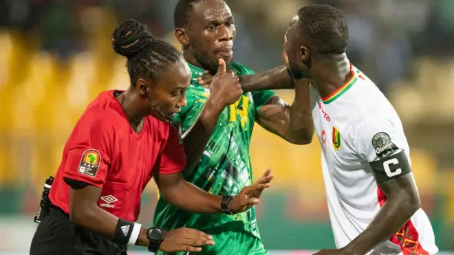 Salma Mukansanga akiranura abakinnyi b'ikipe ya Guinea na Zambia bari bashatse kurwana mu mukino