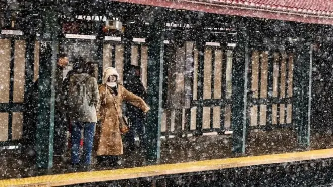 Pipo dey stand on outdoor subway platform as heavy snow dey fall