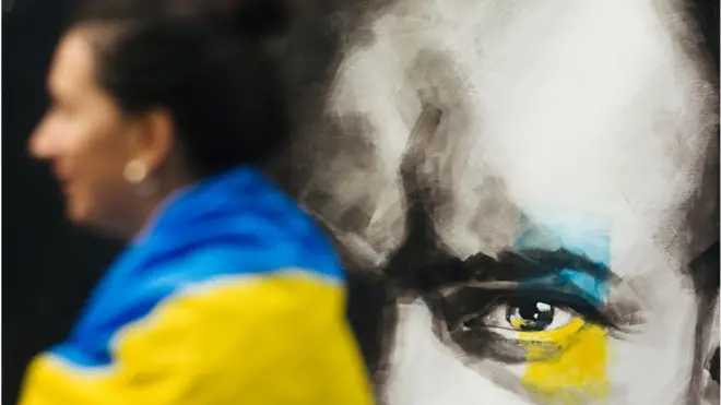 คนคลุมธงชาติยูเครนเดินผ่านภาพวาดบนผนัง