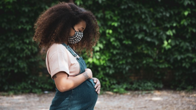 Gestante com máscara segura e acaricia a barriga