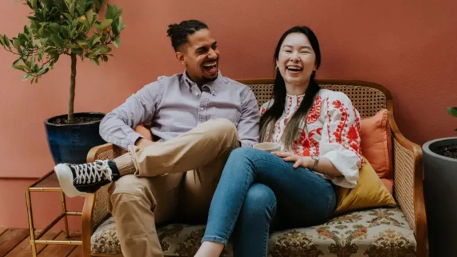 زن و مردی کنار هم روی مبل نشسته‌اند و می‌خندند