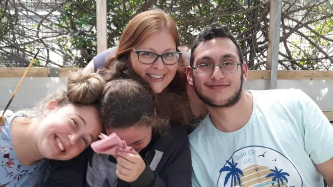 Èèyàn mẹ́rin nínú àwòrán: ọkùnrin kan wà ní apá ọ̀tún, tí obìnrin tó dàgbà tẹ̀le. Àwọn obìnrin méjì wà pẹ̀lú wọn tí ojú ọ̀kan kò hàn.