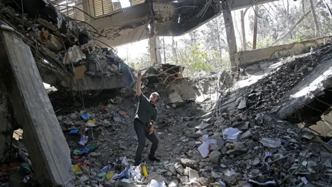 A man stands pointing upwards in the impact site of one of Israel's missiles on the administrative building at Evin Prison, where a large number of people were killed