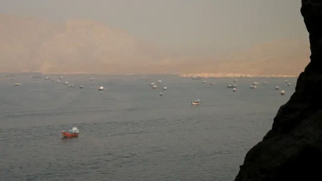 Marinka Hormuz ayaa meel fog laga arkayaa, iyadoo dhowr markab oo shidaal qaada (tankers) iyo maraakiib xamuul ah ay ku sugan yihiin biyaha. Buuro ayaa ka muuqda qeybta hore ee muuqaalka iyo sidoo kale meelaha fogfog ee dambe.