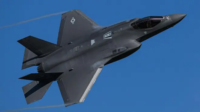 Siyah bir F-35 Lightning II hayalet savaş uçağı açık mavi bir gökyüzünde dönüş yapıyor