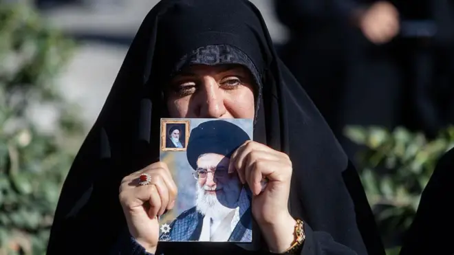 तेहरान में आयोजित शोक समारोह के दौरान एक महिला सर्वोच्च नेता आयतुल्लाह अली ख़ामेनेई का चित्र हाथ में लिए दिखाई दी. ईरान के इस्लामी गणराज्य के समर्थक तेहरान में एकत्र हुए और शोक व्यक्त किया, जब यह ख़बर सामने आई कि सर्वोच्च नेता आयतुल्लाह अली ख़ामेनेई की उनके परिसर पर अमेरिका–इज़राइल के संयुक्त हवाई हमले में मौत हो गई है. ईरानी सरकार ने उनकी मृत्यु की पुष्टि करते हुए 40 दिनों के शोक और सात दिन के राष्ट्रीय अवकाश की घोषणा की. इसके बाद एंगेलाब स्क्वायर और इमाम रज़ा मस्जिद में बड़े पैमाने पर प्रार्थना सभाएं आयोजित की गईं. राज्य मीडिया ने हज़ारों समर्थकों को शोक मनाते हुए दिखाया, जबकि कुछ रिपोर्टों में जनता की मिली-जुली प्रतिक्रिया का भी ज़िक्र किया गया.