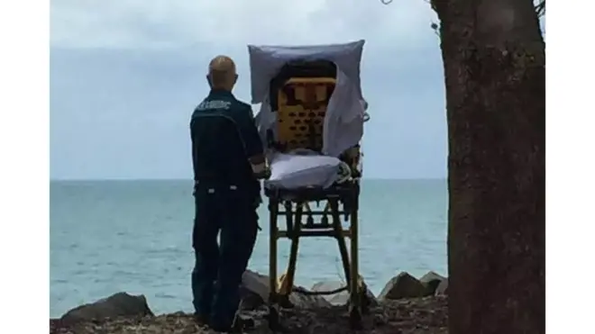 Sedyesinde denize bakan kadın ve solundaki ambulans görevlisi