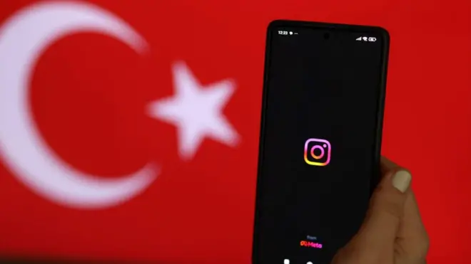 Türk bayrağı önünde, ekranında Instagram logosu olan bir telefon