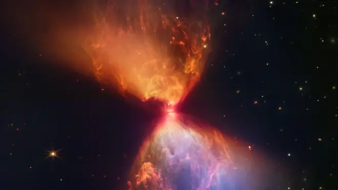 Nubes arremolinadas de color naranja y azul se extienden por encima y por debajo de un centro brillante, con un fondo oscuro de estrellas distantes visibles.