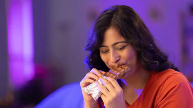 චොකලට් එකක් කමින් සිටින තැඹිලි පැහැති ඇඳුමක් ඇඳ සිටින කාන්තාවක්