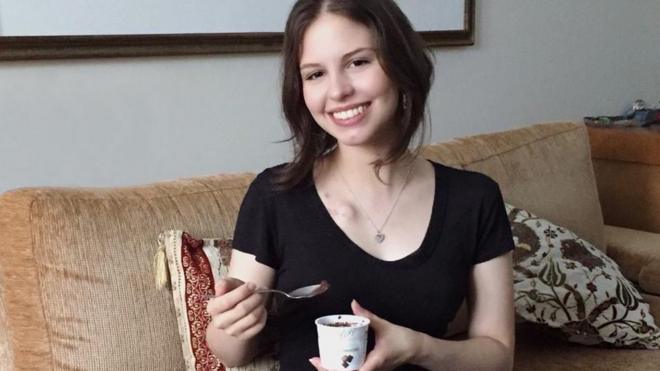 Marcella Cunha sentada em sofá sorrindo e segurando um pote de sorvete
