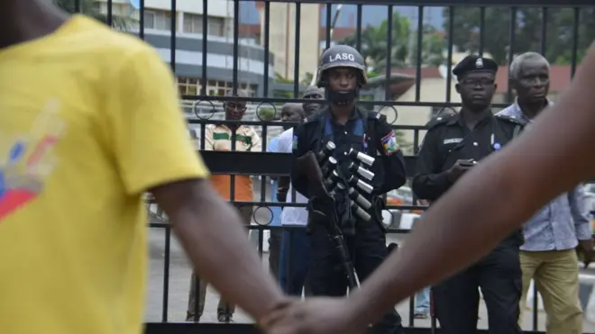 el ele tutuşan göstericiler ve arkalarında silahlı bir asker