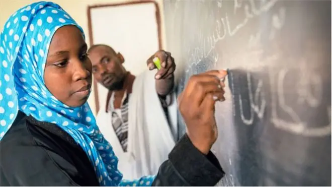 Teacher dey write for board for classroom