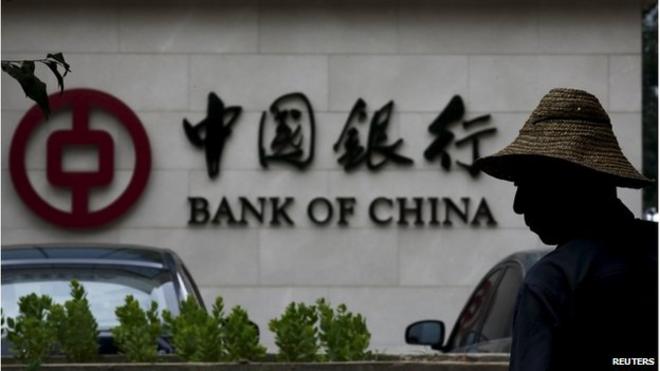 A man is silhouetted in front of a Bank of China"s logo at its branch office in Beijing, in this July 14, 2014 file photo