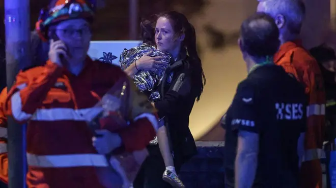 سيدة تحمل طفلاً ملفوفاً ببطانية بعد حادثة إطلاق نار على شاطئ بونداي في سيدني في 14 ديسمبر/كانون الأول 2025
