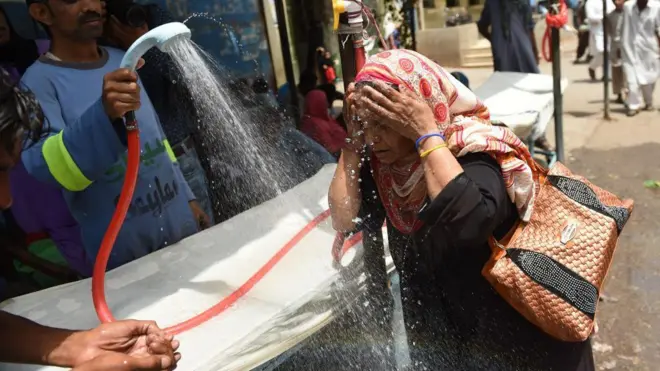 A woman with a headscarf getting sprayed with water.
