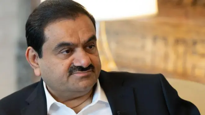 A close-up of Gautam Adani's face wearing a white shirt and black suit jacket during a 2024 interview with Bloomberg news