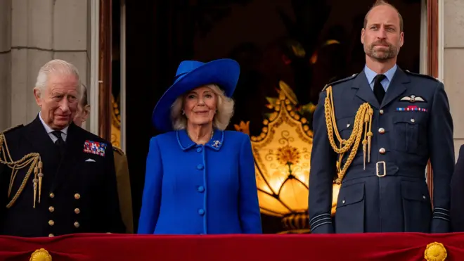 King Charles, Queen Camilla, the Prince and Princess of Wales and their three children look straight ahead on the balcony of Buckingham Palace