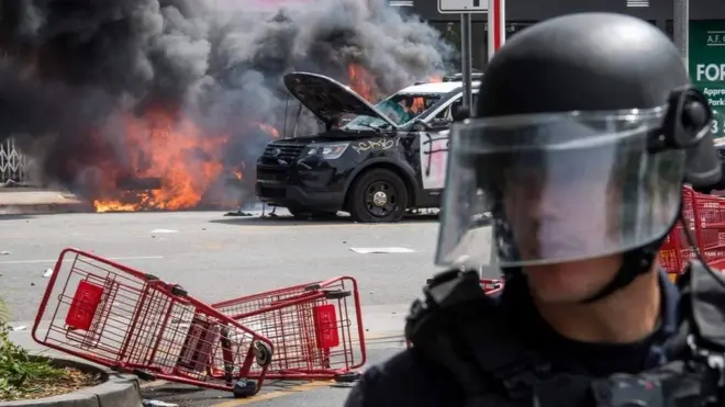 Seorang anggota polisi berjaga-jaga di distrik Fairlax, Los Angeles, setelah pengunjukrasa terlibat bentrokan dengan aparat keamanan, yang ditandai aksi pembakaran mobil polisi.