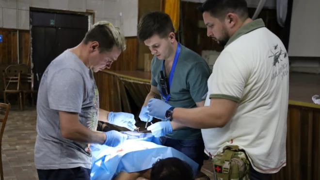Une femme allongée sur une table, le corps recouvert d'un drap d'opération bleu, entourée de trois médecins gantés.