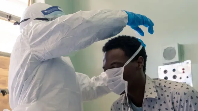Un agent de santé en train de faire porter un masque à un patient au Zimbabwe.