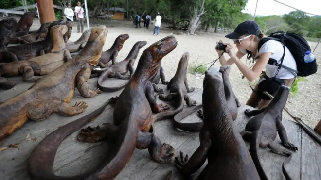 Seorang wisatawan memotret ukiran kayu komodo yang dijual di Pulau Komodo, NTT.